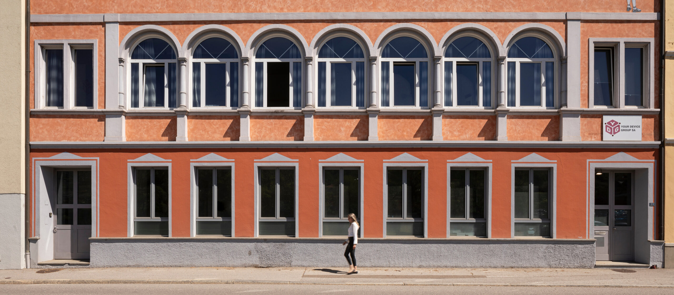 Facciata di un edificio arancione con finestre ad arco e una donna che cammina sul marciapiede